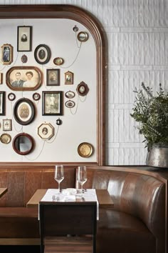 a wall with many framed pictures on it and two wine glasses sitting on the table