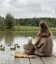 a woman and her child are sitting on a dock watching ducks in the water,