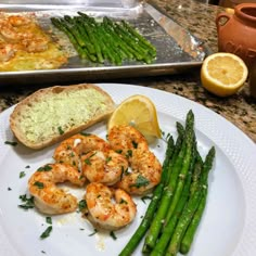 shrimp, asparagus and bread on a plate with lemon wedges next to it