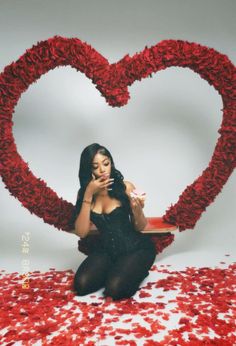 a woman sitting in front of a heart made out of red flowers holding a cell phone