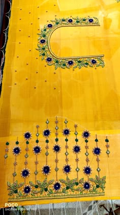 an embroidered yellow cloth with blue flowers and green leaves on the edges is being displayed