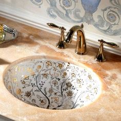 a bathroom sink with an artistic design on the bowl and gold faucet handles