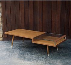 a wooden table with glass top sitting in front of a brick wall and wood paneling