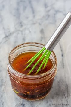 a glass jar filled with sauce and green onions on top of a marble countertop