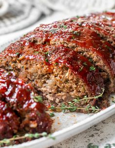 meatloaf with sauce and herbs on a white platter, ready to be eaten