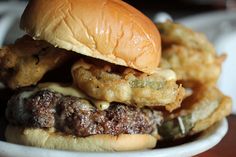 a hamburger with onion rings and cheese on it sitting in a bowl next to some fries