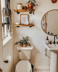 a white toilet sitting next to a sink in a bathroom under a mirror and potted plant