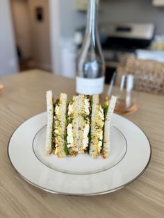 a white plate topped with cut in half sandwiches next to a bottle of wine on top of a wooden table