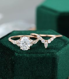 two gold rings with diamonds sitting on top of a green velvet ring box next to each other