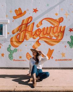 a woman sitting on the ground in front of a wall with words painted on it