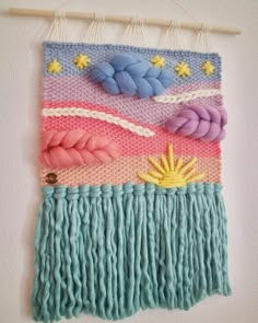 a wall hanging made out of yarn with flowers and leaves on the bottom, in pastel colors