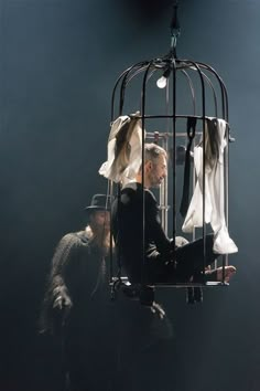 a man sitting in a birdcage with clothes hanging from it's sides