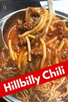 a spoon full of noodles with meat and sauce on it in a bowl next to a red sign that reads hillbilly chili