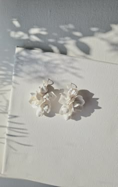 two pairs of white flower earrings sitting on top of a piece of paper