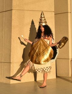 a woman dressed up as a gold witch holding a large golden object in her hand