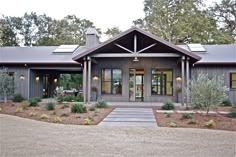 a large gray house with lots of windows and plants on the front lawn, surrounded by trees