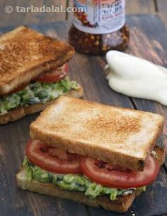 two grilled sandwiches with tomatoes, lettuce and mayonnaise on a wooden table