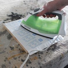 a person ironing something on top of a sheet of paper with a green and white iron