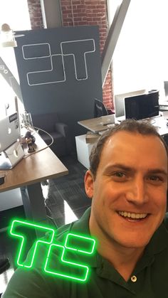 a man sitting in an office with a neon sign above his head that says it