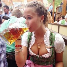 a woman drinking beer while sitting at a table with other people in the back ground