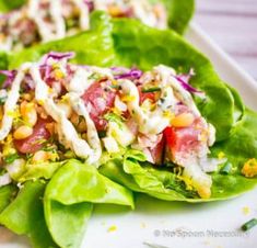 two lettuce wraps filled with meat and vegetables on a white plate next to a knife