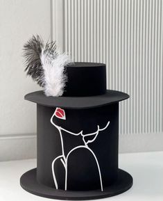 a black top hat with a white feather on the side and an image of a woman's face painted on it