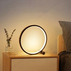 a round light sitting on top of a wooden table next to a vase with flowers