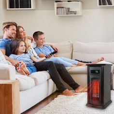 a group of people sitting on a couch watching something in the air with an electric heater