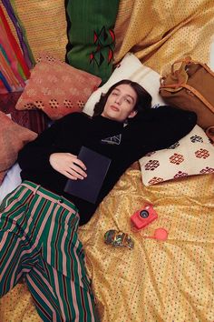 a woman laying on top of a bed covered in blankets and pillows next to a laptop computer