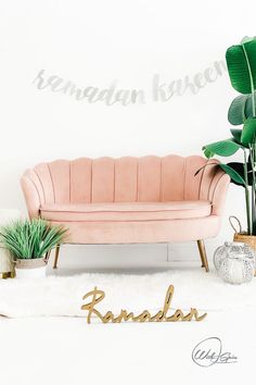 a pink couch sitting on top of a white rug next to a potted plant