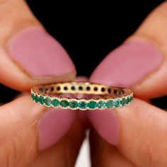 a woman's hand holding a ring with emeralds on it