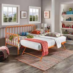 an orange metal bed frame sitting on top of a wooden floor next to two windows