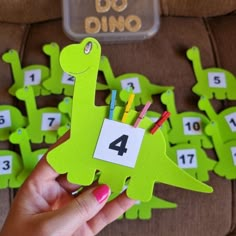 a person holding up a green dinosaur shaped card with numbers and pencils in it