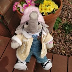 a small stuffed elephant sitting next to a potted plant with flowers in the background