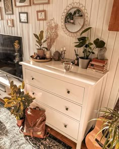 a white dresser sitting in front of a fireplace with potted plants on top of it