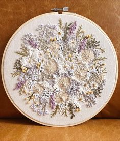 a close up of a cross stitch pattern on a brown leather surface with white and purple flowers in the center