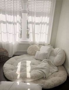 a large round bed in front of a window with white curtains and pillows on it