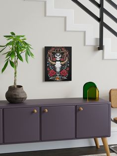 a painting on the wall next to a purple cabinet with a potted plant in it