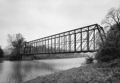 a black and white photo of a bridge over a body of water with trees in the background