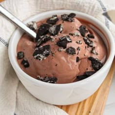 a white bowl filled with chocolate ice cream and oreo chunks on top of a wooden cutting board