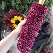 a hand holding a crocheted wine bottle cover in front of a sunflower