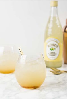 two glasses filled with liquid sitting on top of a table next to bottles and utensils