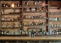 the bar has many bottles on it and is lined with shelves full of liquors