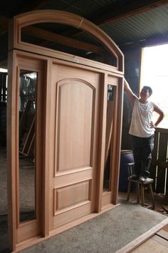 a man standing next to a wooden door on top of a hard wood floor in front of a window