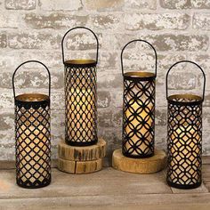 three metal lanterns sitting next to each other on top of a wooden stand with a brick wall in the background