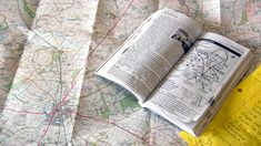 an open book sitting on top of a map next to a yellow piece of paper