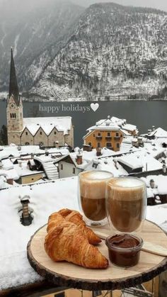 two glasses of coffee and croissants on a table with snow covered mountains in the background