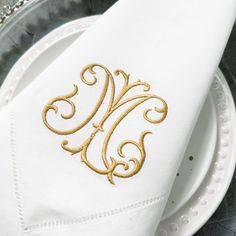 a white plate topped with a napkin and gold monogrammed initial on top of it