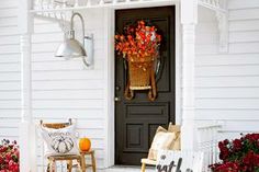 the front porch is decorated for fall with pumpkins and flowers on the table, along with two chairs