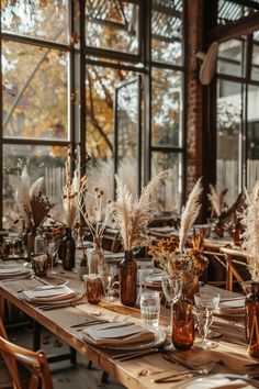 the table is set with place settings and vases filled with dried flowers, grasses, and candles